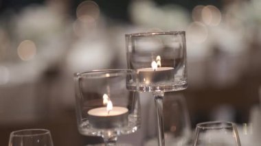 Zarif cam tutacaklarda, yumuşak bir arka planı olan iki mum yakın. Statik çekim.