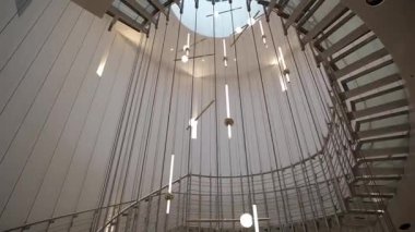 27 Kasım 2024 'te Westin Varşova Oteli' nin avlusundaki ikonik cam spiral merdiven ve modern asılı ışık heykelinin alçak açılı görüntüsü.