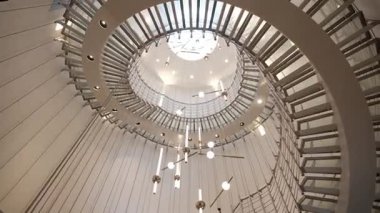 WARsaw, POLAND - 27 Kasım 2024: Batı Varşova Oteli 'nin lobisinde modern cam spiral merdiven ve çağdaş ışık kurulumunun düşük açılı iç görünümü