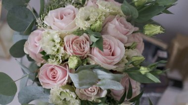 Gümüş okaliptüs yapraklı, yumuşak pembe güller ve beyaz lisianthus aksanlı romantik bir gelin buketi.