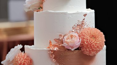 Şeftalili yıldız çiçekleri ve gül sarısı folyo aksanıyla süslenmiş üç katlı zarif düğün pastası.