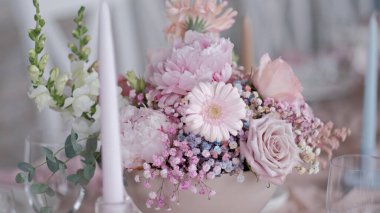 Süslü bir düğün masasında pembe papatyalar, şakayıklar ve güllerle süslü pastel çiçek aranjmanı.