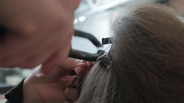Müşterinin doğal saçlarına keratin saçı eklemek için özel pense kullanan profesyonel bir saç stilisti.