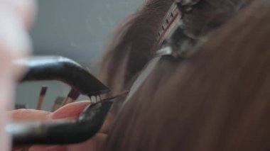 Kuaför keratin senedi uygulaması için koruyucu kalkan şablonuna ince bir saç teli yerleştiriyor. Yakın çekim.