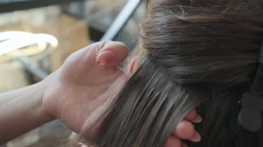 Profesyonel stilist, bir güzellik salonunda uzun kahverengi saç tellerini uzatma işlemi için ayırıyor.