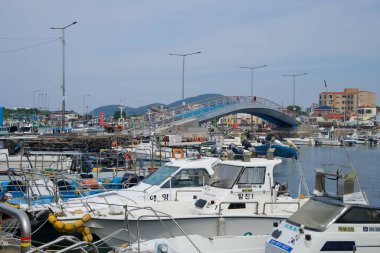 Mavi kemerli bir yaya köprüsü Hwabuk limanını geçerken sokak lambaları ve bazalt rezervasyonlarının altındaki ön taraftaki küçük balıkçı tekneleri ve teçhizatları dolduruyor..