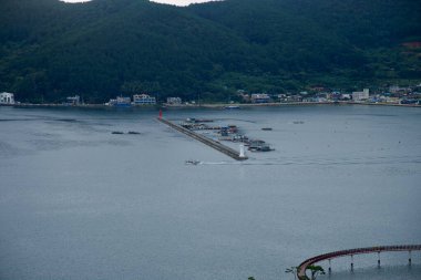 Küçük bir balıkçı teknesi Jisepo Limanı 'ndan ayrılır ayrılmaz dalgakırandaki beyaz deniz fenerini geçerek alçak ormanlık tepeler, dağınık evler ve uzaktaki eğimli sahil parkı görünür hale gelir..