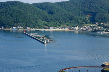 İkiz deniz fenerleri Jisepo Limanı dalgakıranının sonunu işaret ediyor. Balıkçı tekneleri ve tekneler sakin körfezin arkasında toplanıyor..