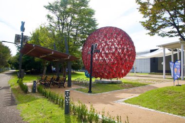 Chuncheon 'daki Animasyon Müzesi çimlerinin altında bronz köy temalı bir heykel duruyor. Etkinlik afişleri ve çimenlerin üzerinde kırmızı kurdele küreleri görülüyor..