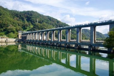 Uiam Barajı, Kuzey Han Nehri 'nin bir kıvrımında uzanır. Devamlı sütunları, alçak tepeler ve dağınık bulutlarla durgun sularda yankılanır..