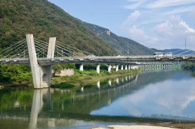Gangchon Grand Köprüsü 'ndeki kablo destekli direklerin yakın görüntüsü trafik Bukhangang' ı dar bir vadiden geçerken, otobüsler ve arabalar üstümüzden geçerken ve yumuşak yansımalar altında.