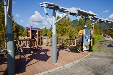 Bisiklet rafları Kyunggang Köprüsü sertifika standının yanındaki güneş paneli gölgesinin altında duruyor. Bukhangang yakınlarındaki Gapyeong 'da nehir kenarında sonbahar ağaçları var..