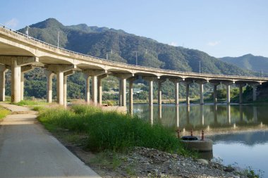 Cheongpyeong yakınlarındaki Bukhan Nehri 'nin üzerindeki beton viyadük kıvrımları, ağaçlık dağ yamaçlarının altındaki setlerin yanındaki sığ sulara yansıyor..