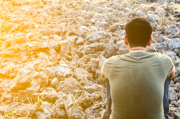 Frustrated and sad young man sitting in barren ground. with sun light — Stock Photo, Image