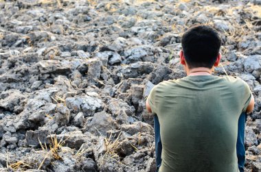 Hayal kırıklığına uğramış ve üzgün genç adam çorak yere oturuyor. Bir kuru pirinç alan için Görünüm.