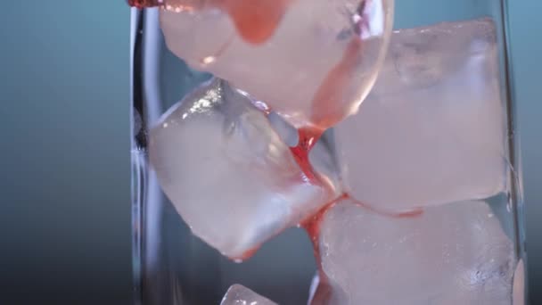 Closeup of red syrup pouring  over ice in glass — Stock Video