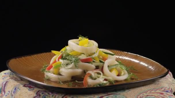 Салат з кальмарами на тарілці, що вивертається на чорному фоні — стокове відео