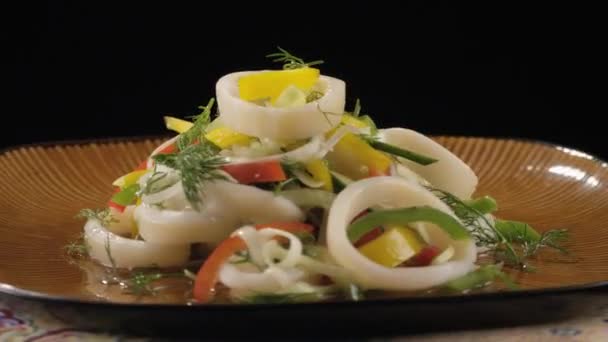 Salade met inktvis op een schotel draaien op zwarte achtergrond — Stockvideo