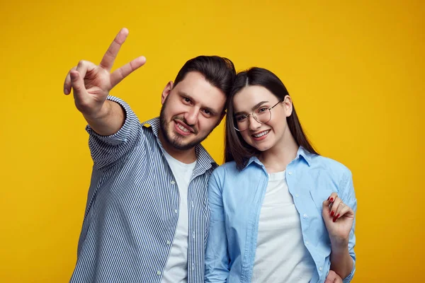 Felice coppia sorridente e mostrando gesto di pace su sfondo giallo — Foto Stock