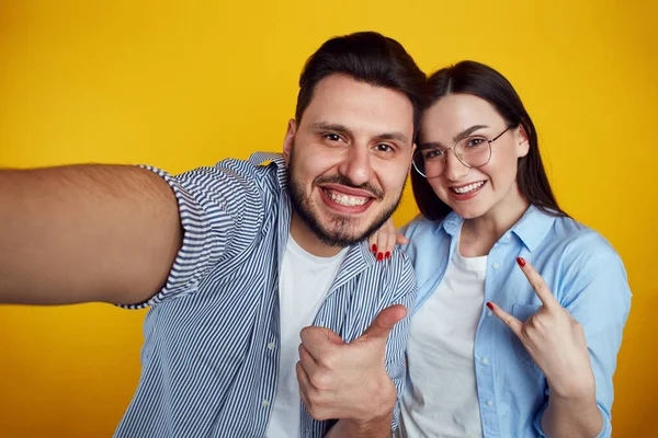 Coppia prende selfie sul cellulare, fa come gesti su sfondo giallo — Foto Stock