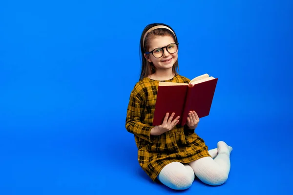 Criança feliz sorrindo enquanto sentado contra fundo azul e livro de leitura — Fotografia de Stock
