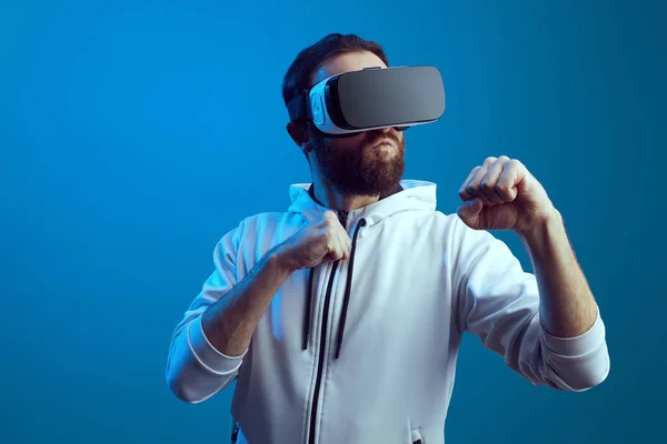 Young man in modern VR device standing in boxing position over blue wall — Stock Photo, Image