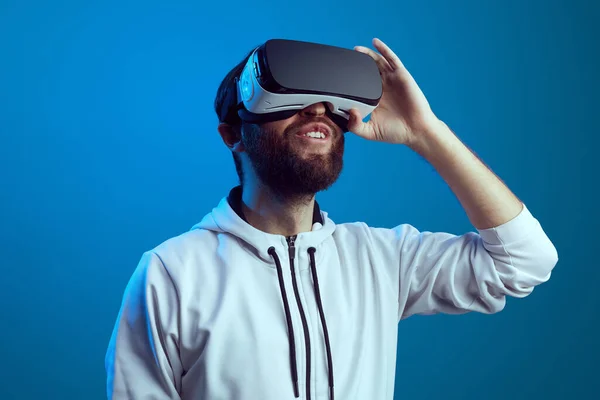 Homem barbudo desfrutando de óculos de realidade virtual contra fundo azul — Fotografia de Stock