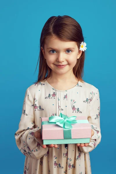 Gadis kecil yang mendemonstrasikan kotak hadiah yang dibungkus dengan pita menghadap dinding biru — Stok Foto