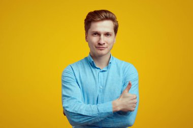 Kendine güveni tam, mavi tişörtlü, başparmağıyla işaret eden yakışıklı adam.