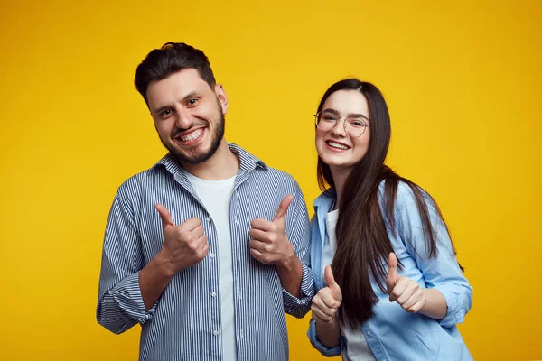 Mutlu çift gülümsüyor ve sarı arka planda başparmak gösteriyor.