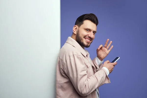 Homem de pé ao lado de parede de cartaz branco vazio e mostrando gesto ok — Fotografia de Stock