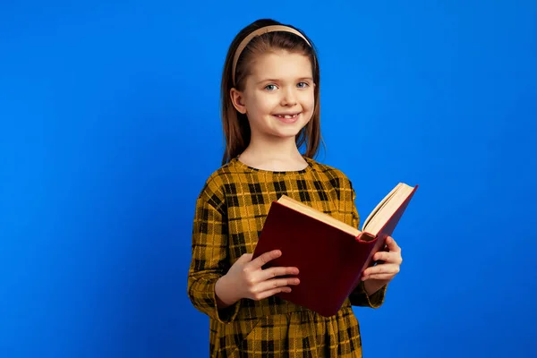 Criança feliz sorrindo e segurando um livro contra fundo azul — Fotografia de Stock