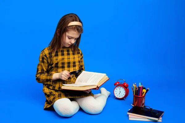 Criança inteligente usando lupa para ler o livro durante os estudos — Fotografia de Stock