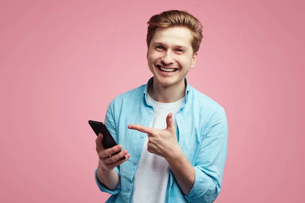 Hombre satisfecho en camisa azul, puntos con el dedo índice en el dispositivo de teléfono inteligente — Foto de Stock