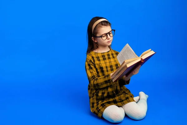 Criança feliz ler livro e sentado contra fundo azul — Fotografia de Stock