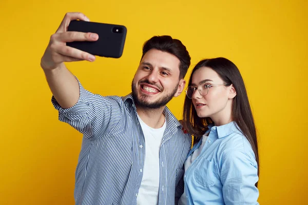 Uomo e ragazza scattare selfie in studio, isolato su sfondo giallo — Foto Stock