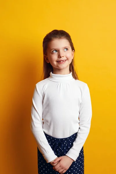 Gülümseyen genç kız, düşünceli bir şekilde sarı arka plana bakıyor.