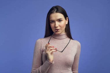 Ciddi derecede çekici sakin öğrenci kız ağzının kenarında gözlük tutuyor.