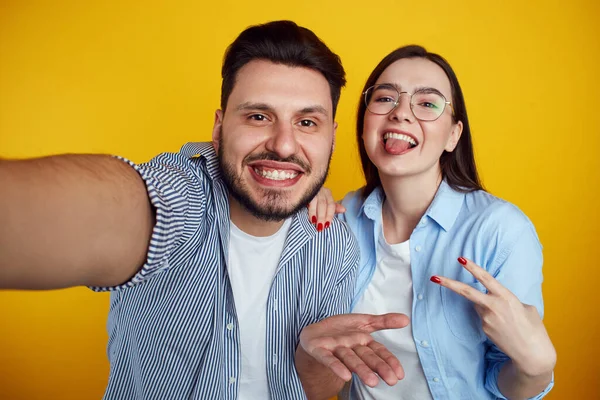 Mężczyzna i dziewczyna biorąc selfie w studio, izolowane na żółtym tle — Zdjęcie stockowe