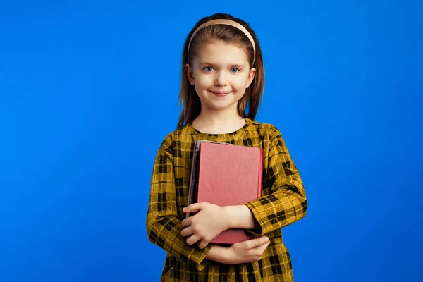 Pequena colegial em vestido casual segurando livros contra fundo azul — Fotografia de Stock