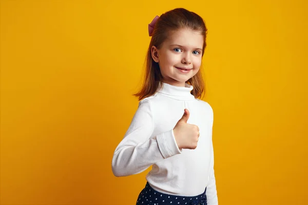 Menina garoto otimista mostrando polegares para cima contra fundo amarelo brilhante — Fotografia de Stock