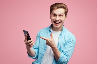 Mavi gömlekli tatmin olmuş erkek, akıllı telefon cihazına işaret parmağıyla işaret ediyor.