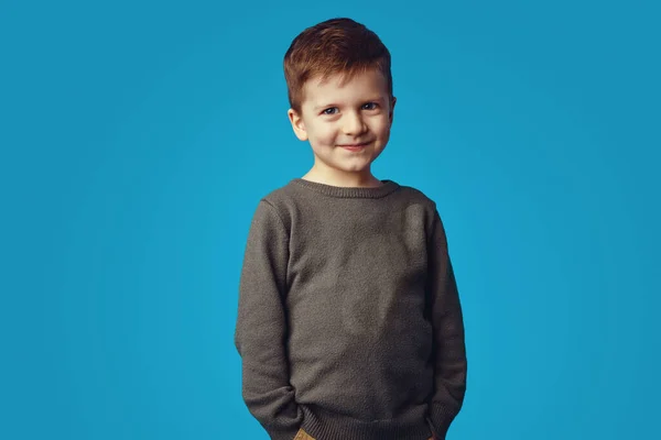 Дитина посміхається, тримаючи руки в кишенях, ізольовані на синьому фоні — стокове фото
