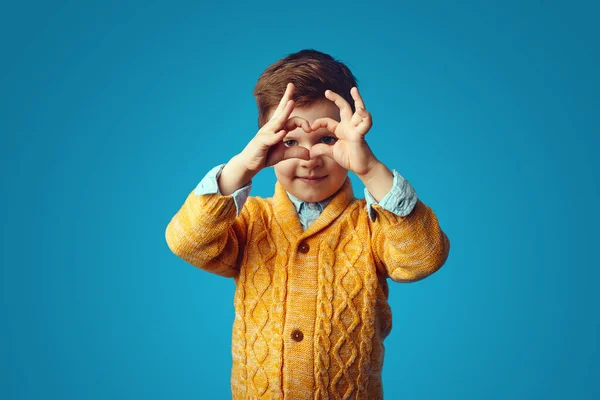 Cute lovely kid wearing yellow cardigan, showing a heart shape with hands — Stock Photo, Image