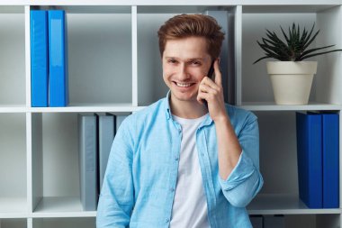 Ofiste dururken akıllı telefondan konuşan çekici bir genç.