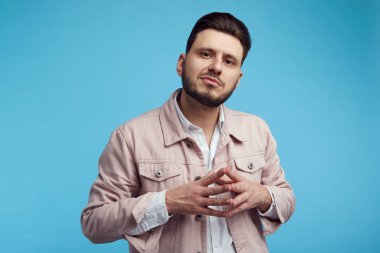 Ciddi adam ellerini birbirine bastırır, mavi arka planda soyutlanır.