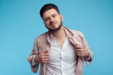 Kendini özel ve yakışıklı hisseden bir adam, mavi stüdyo geçmişine karşı duruyor.