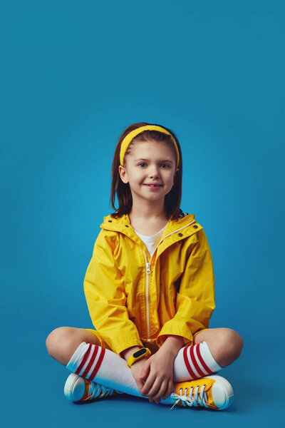Girl in bright yellow outfit, smiling at camera while sitting cross legged