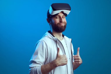 Alnında VR gözlüklü adam mavi arkaplan üzerinde başparmak gösteriyor