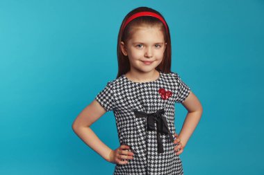 Küçük sevimli kız gülümsüyor ve ellerini mavi duvarın üstünde tutuyor.